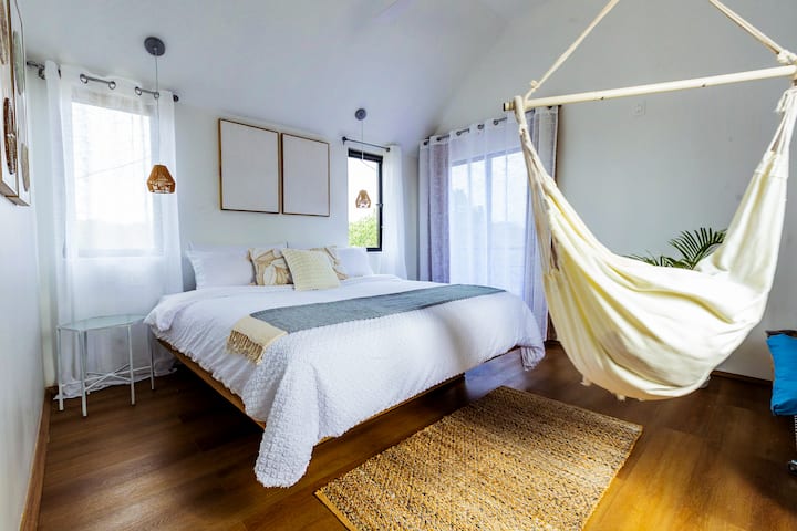 A calming bedroom designed to help you rest and recharge—complete with a private balcony, hammock chair, and minimalist clothing rack—where mornings feel light and unhurried. 