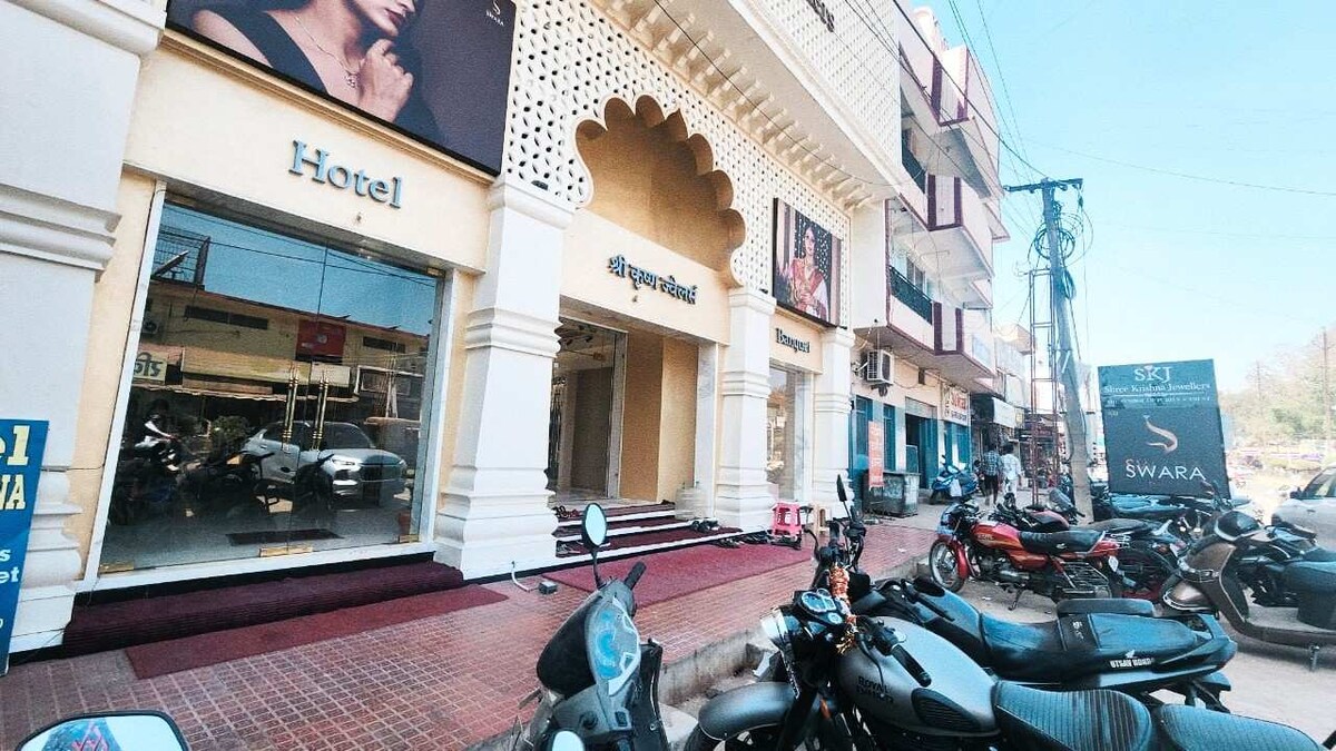 The hotel exterior is characterized by an archway entrance, complemented by decorative elements and large windows. The façade features promotional images and signage, while several parked motorcycles line the street in front, providing a glimpse of the bustling atmosphere.
