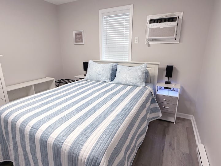 Back bedroom features queen bed, side table, dresser, and AC wall unit.