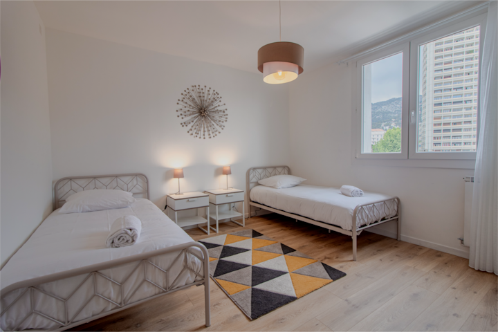 Поглед кон втората спална соба со два одделни единечни кревета, секој опремен со постелнина и крпа. Две ноќни масички со нагласени ламби. Голем прозорец со навалување и вртење со двојно стакло со непречен поглед.