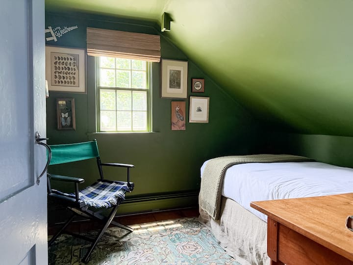 Bedroom with twin bed upstairs with fun vintage camp decor. All bedrooms have luxury mattresses, pillows, and linens. Bedside table has reading lamp and charging port for convenient device charging. 
