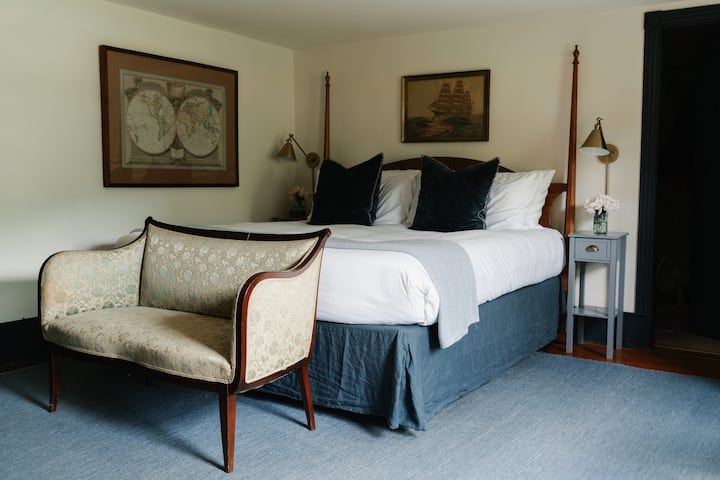 Our "Captain's Quarters" primary king bedroom on ground floor with luxury mattress and linens. Each bedside table has a lamp and charging ports for devices. 
