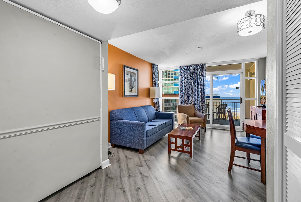 مساحة معيشة مشرقة وجذابة مع أرضيات حديثة ومقاعد مريحة ووصول مباشر إلى شرفة خاصة توفر إطلالات على المحيط.