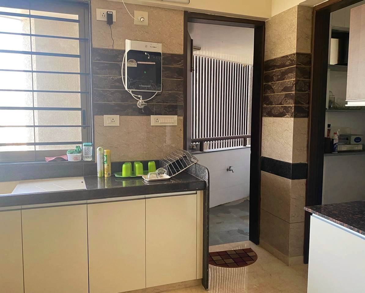 The kitchen area features modern appliances with a sleek countertop and storage cabinets. A small dish drying rack is positioned next to the sink. Natural light enters through a window with horizontal bars, illuminating the space.