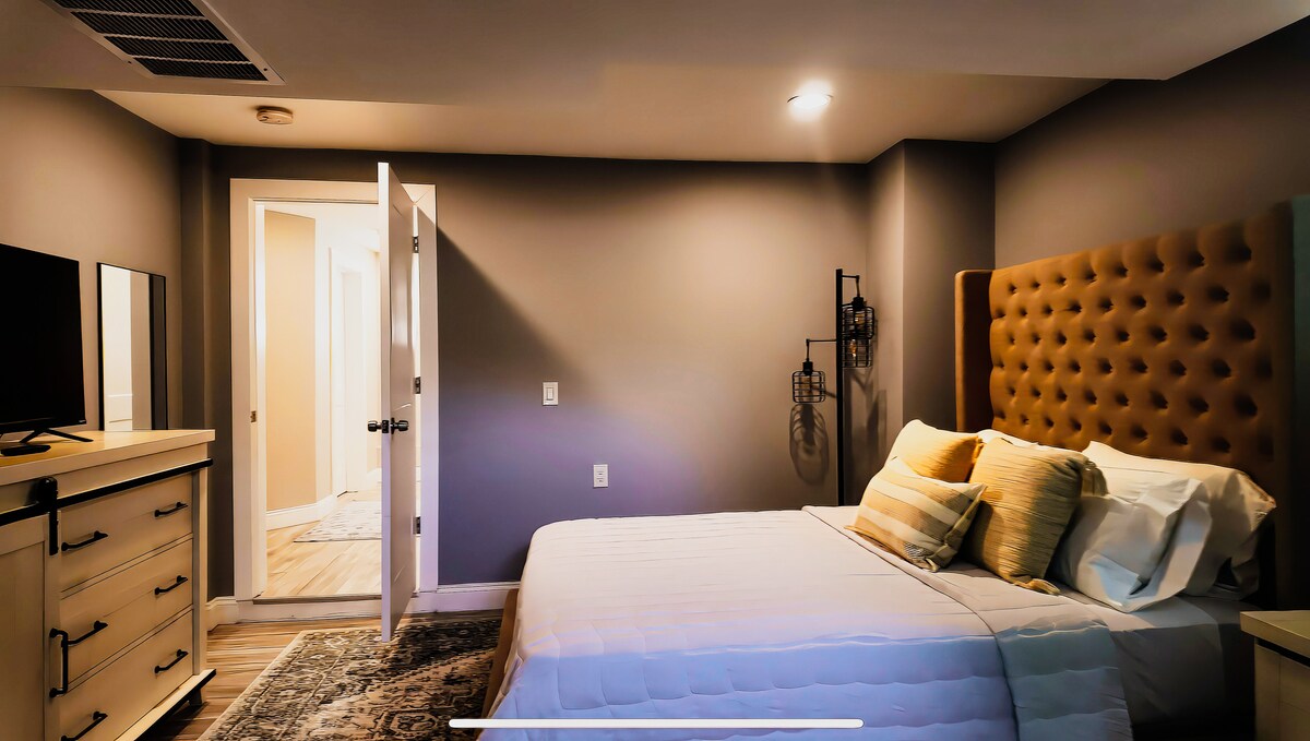 Chambre moderne et minimaliste à la lumière du jour – Des murs neutres et doux, de la literie claire et de grandes fenêtres créent une atmosphère lumineuse et aérée.