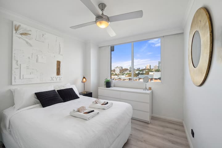 Moderna spavaća soba s ventilatorom, bijelim zidovima i krevetom s ručnicima.