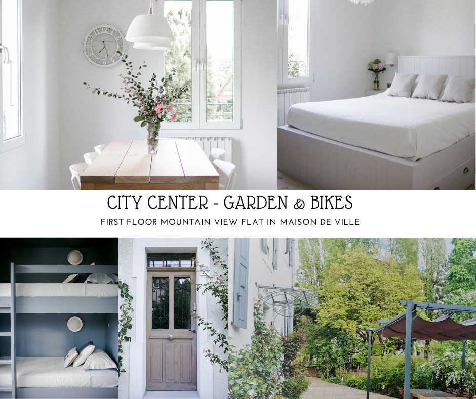 The image showcases a bright and airy dining area with a wooden table adorned by a vase of flowers, alongside a spacious sleeping area featuring a large bed against a neutral backdrop. A blue-gray built-in bunk bed occupies the corner, and the outdoor garden displays lush greenery and a pergola.
