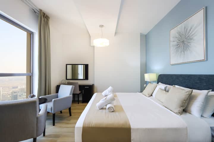 მსხვილი, მზით განათებული საძინებელი თანამედროვე ავეჯითა და ქალაქის ხედით
