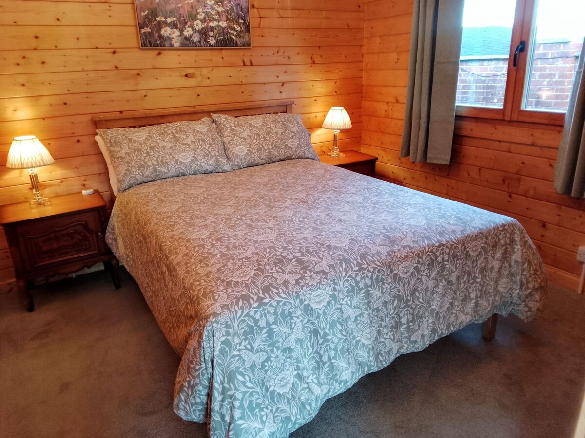 Затворената спална соба во задниот дел на дрвената колиба има стандарден двоен кревет плус две ноќни масички со ламби.  Удобните дебели теписи и покривката од природно дрво гарантираат дека добро ќе се наспиете. 