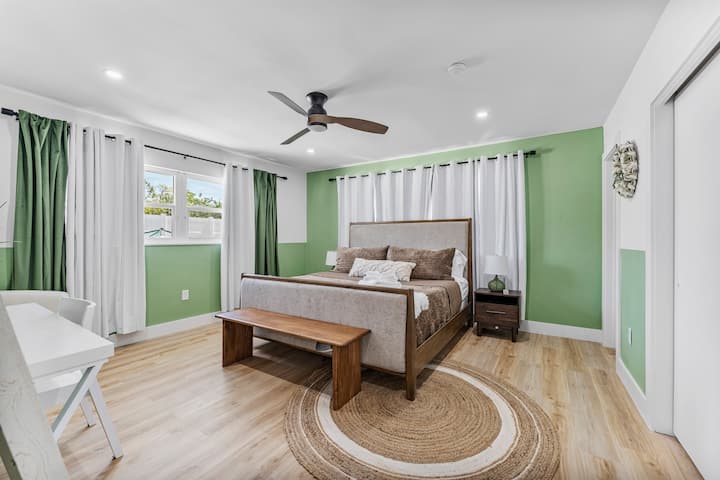 Relax in this spacious bedroom with calming green accents, a plush king-size bed, and modern decor – perfect for unwinding after a day at the beach.