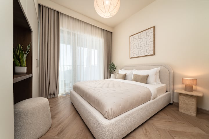 Një dhomë gjumi elegante me një krevat të rehatshëm, mobilie moderne dhe dritare nga dyshemeja në tavan që ofrojnë pamje mahnitëse të qytetit, si ditën ashtu edhe natën.