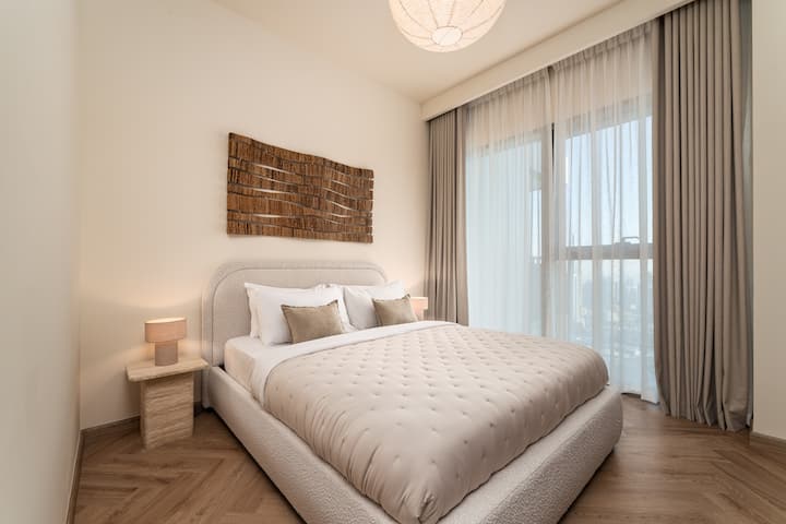 Një dhomë gjumi elegante me një krevat të rehatshëm, mobilie moderne dhe dritare nga dyshemeja në tavan që ofrojnë pamje mahnitëse të qytetit, si ditën ashtu edhe natën.