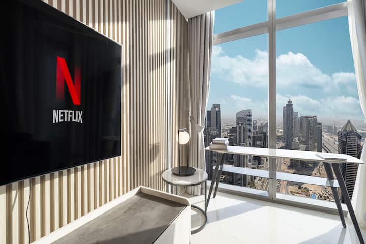 En mysig arbetsyta med ett modernt skrivbord och en elegant svart stol placerad vid stora fönster, med panoramautsikt över staden. Väggen har en platt-TV och rummet är inrett i en minimalistisk stil.