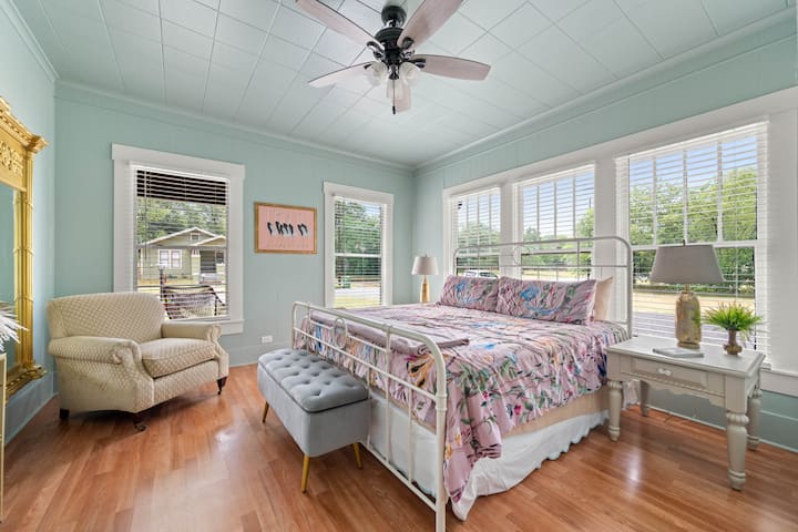 Bedroom with King Bed, TV, Full Body Mirror and Cozy Reading Chair, extra blankets in the storage bench, room darkening blinds, ceiling fan, large closet with hangers, kids play mat, extra sleeping cot and an extra fan.