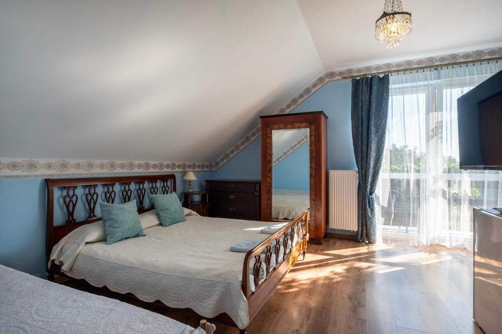 A well-lit bedroom features a spacious bed with soft linens and decorative pastel pillows. A wooden mirror complements the room, alongside a chest of drawers. Natural light filters through sheer curtains, illuminating the warm wooden flooring and creating a serene ambiance.