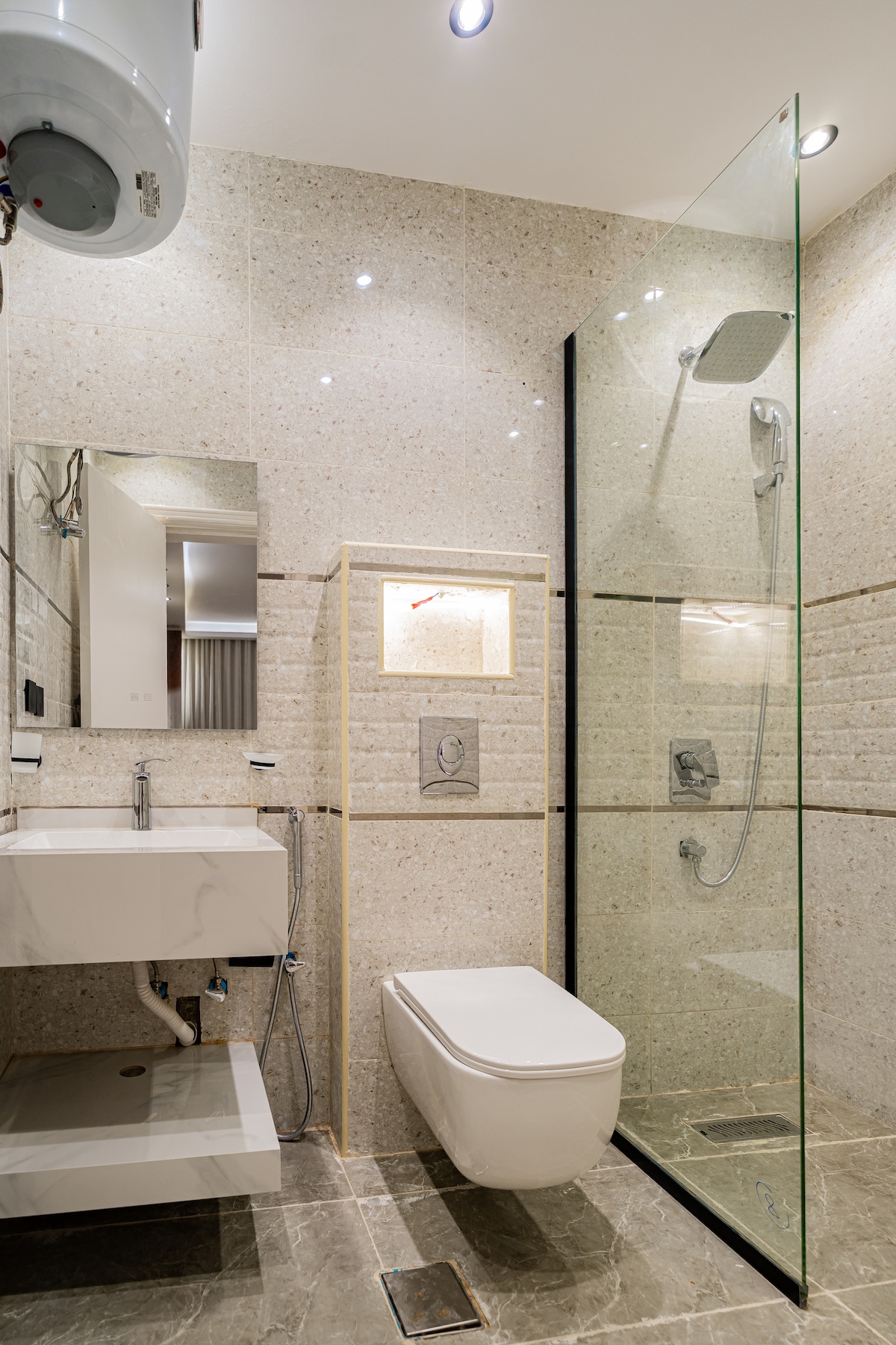 A modern bathroom is displayed, featuring a glass shower enclosure with a handheld showerhead. A sleek white toilet and a contemporary sink with a mirror above are included. Neutral-toned tiles cover the walls, while recessed lighting offers ambient illumination.