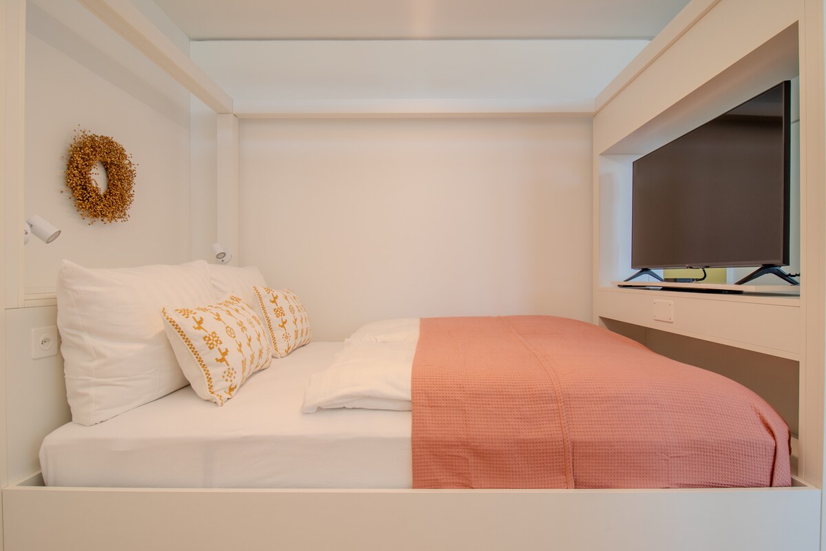 חדר שינה נעים במודול MOVEment עם מיטה זוגית נוחה, צבעים חמים וטלוויזיה משולבת. מושלם ללילות רגועים באווירה מודרנית ושקטה.