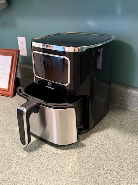 An air fryer is positioned on a kitchen countertop. The appliance features a sleek black exterior with a stainless steel drawer handle. A digital display panel is located on the front, providing a modern touch to the kitchen space.