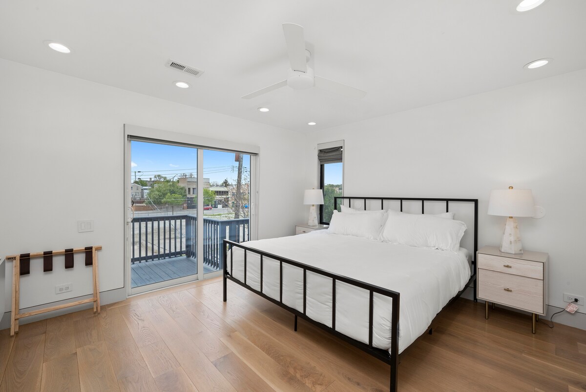 Dormitorio principal luminoso y sereno con una cama tamaño king con sábanas blancas frescas, mesitas de noche modernas y pisos de madera cálidos. Las puertas corredizas se abren hacia un balcón privado, perfecto para el café de la mañana o un momento tranquilo juntos en un refugio tranquilo.