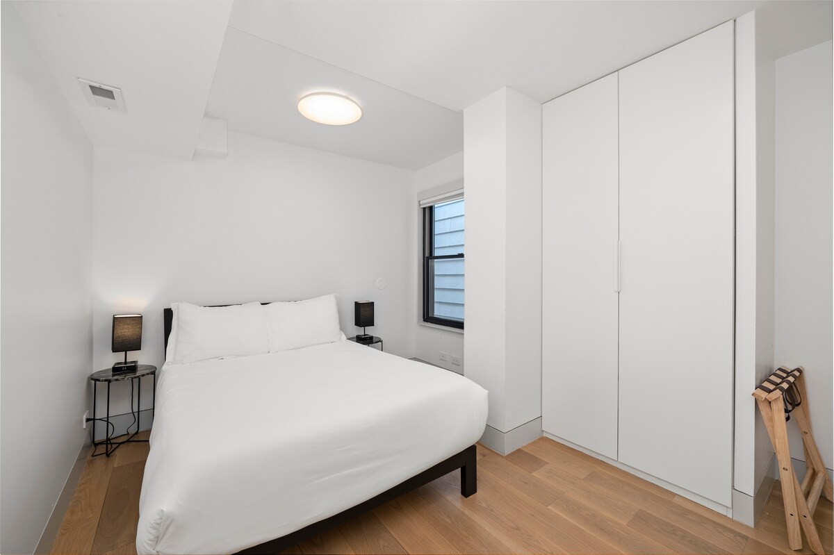 Dormitorio acogedor y moderno con cama de matrimonio, armario empotrado y decoración minimalista. La iluminación suave, los cálidos suelos de madera y una tranquila vista de la ventana lo convierten en un lugar tranquilo para descansar y relajarse.
