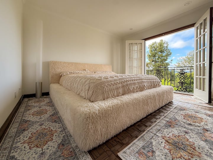 Rilassati in un letto matrimoniale grande da sogno con una morbida cornice in finta pelliccia e lenzuola di lusso. Luci d'accento di design e porte finestre si aprono su viste panoramiche, creando un rifugio tranquillo ed elegante. Perfetto per notti riposanti e mattinate tranquille.