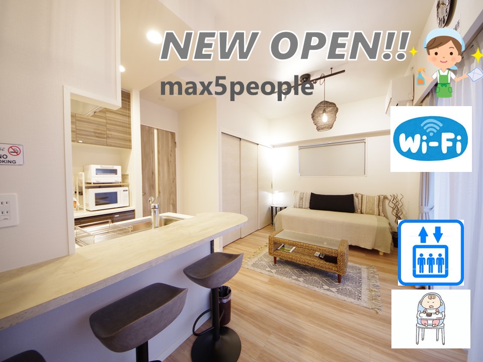 An open-concept living area features a light-colored sofa and a wooden coffee table. The kitchen area is equipped with modern appliances, including a microwave. Bright natural light enters through large windows, enhancing the welcoming environment. A minimalistic design is complemented by wooden accents.