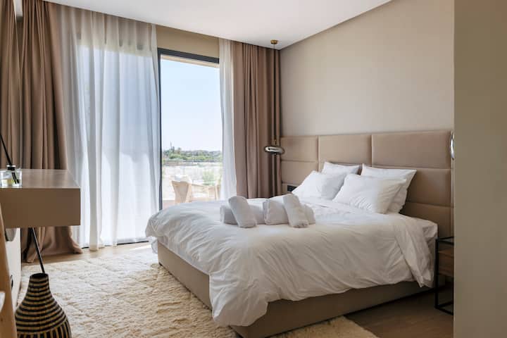 חדר מואר עם גישה ישירה למרפסת.
מיטה זוגית עם מצעי כותנה פרימיום, וילונות האפלה ופתיחה לאזור חיצוני פרטי.