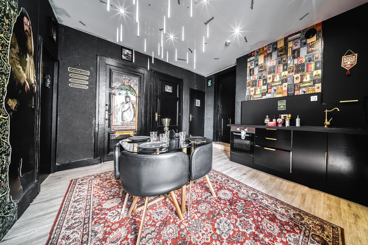 An elegant dining area is featured with a stylish black table surrounded by four chairs. The room is enhanced by a patterned rug and ambient lighting from hanging fixtures. A black cabinetry unit displays various decorative items and a wall adorned with colorful artwork adds character.
