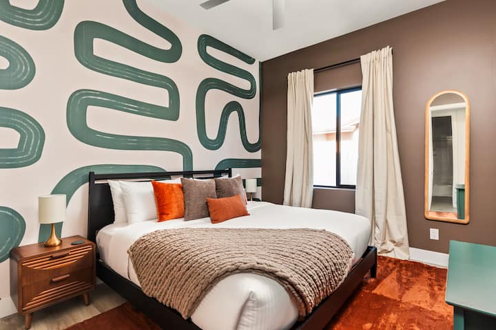 ️ Chic bedroom featuring a bold accent wall, cozy bedding, and pops of earthy tones. Modern side tables, soft lighting, and natural sunlight create a stylish yet calming retreat, perfect for unwinding after a day of adventure.
