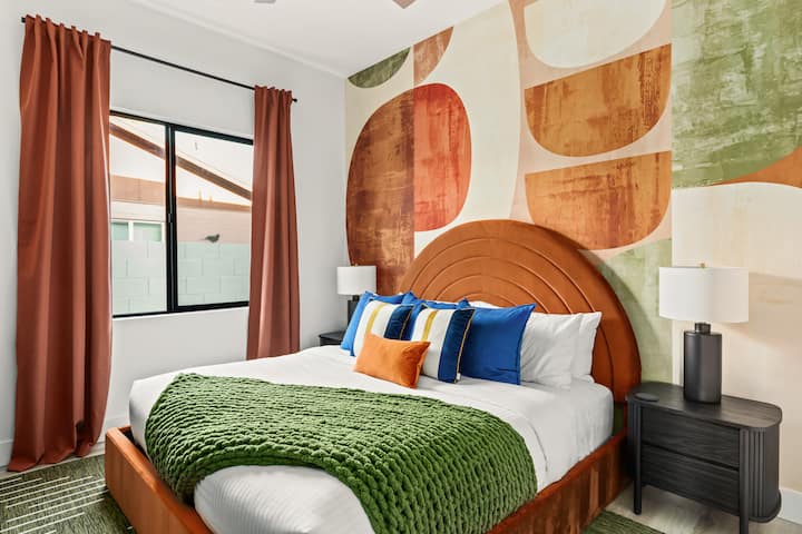 ️ Vibrant bedroom with bold accent wall, cozy bed, and soft layered pillows. Warm tones, blackout curtains, and modern lamps create a stylish yet relaxing retreat. Perfect for restful sleep and a colorful touch to your stay.