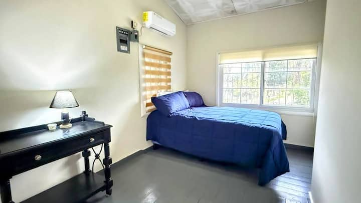 Cómoda habitación con cama queen, ideal para parejas o viajeros solos. Espacio acogedor con decoración minimalista, persianas blackout, mesa lateral con lámpara y un ambiente tranquilo perfecto para descansar tras un día de playa.