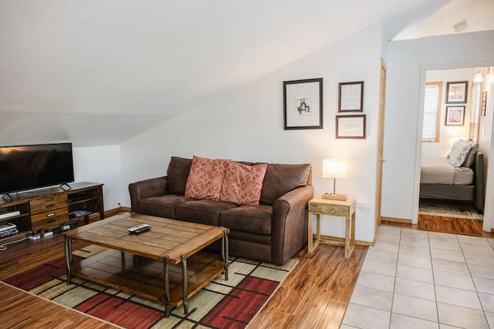 Living room with TV, couch, coffee table that will have your FAQs + local's guide, rocking chair for additional seating, and featuring a lamp where you can charge all your devices.