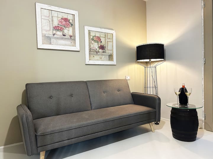 ספה עם שולחן קטן, בקבוק יין וכוסות, פריטי נוי על הקירות