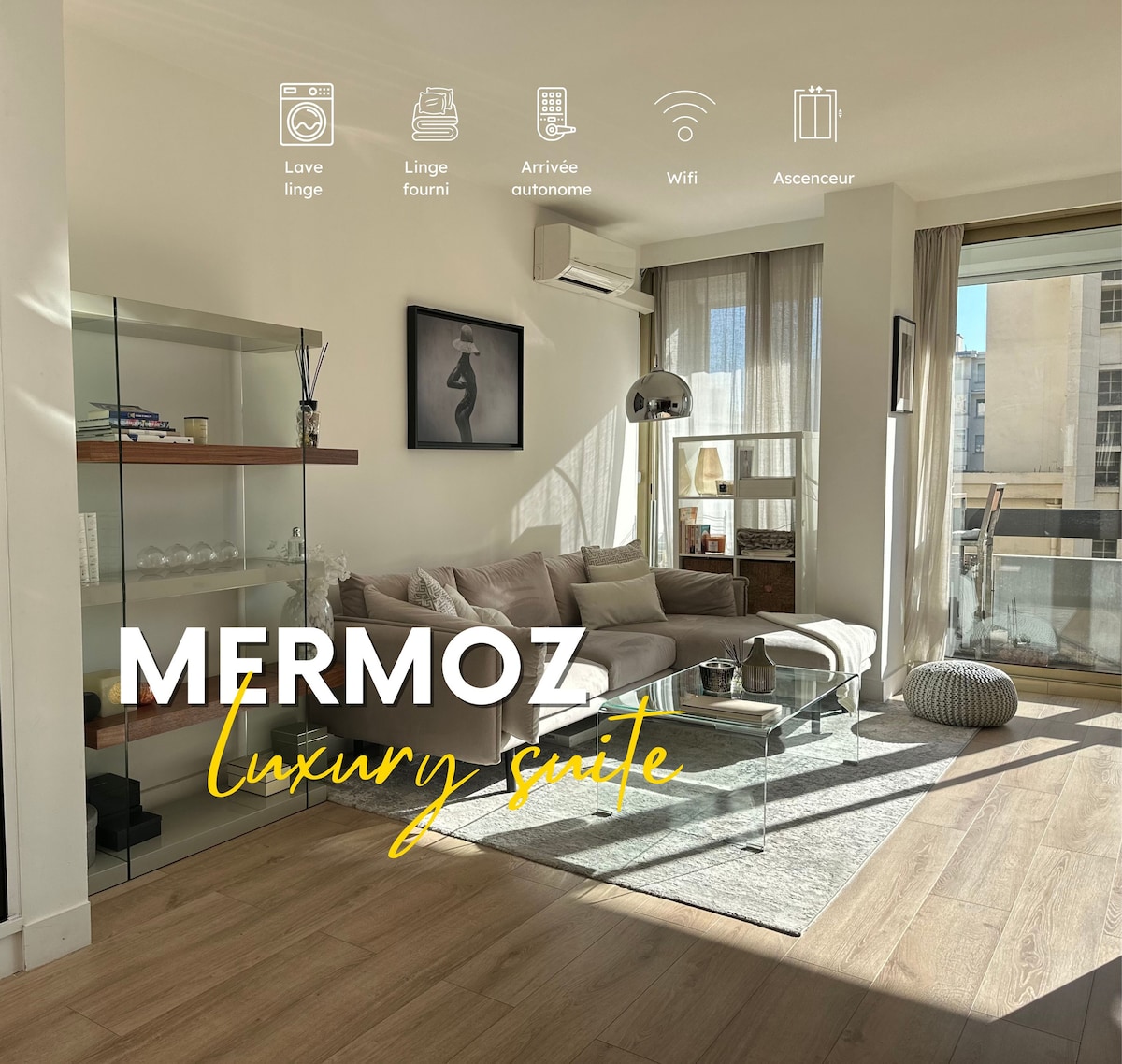 A bright living space features large windows that allow natural light to flow in. A glass coffee table sits on light wood flooring, accompanied by minimalistic shelving. An art piece adorns the wall, while a comfortable seating area invites relaxation.