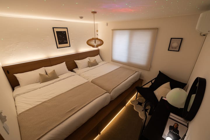 Es un dormitorio con dos amplias camas tamaño queen en un piso elevado, un interior moderno y una iluminación aurora que añade un ambiente sutil.
Disfruta de un descanso especial en este espacio donde la calidez y la sofisticación coexisten. ✨