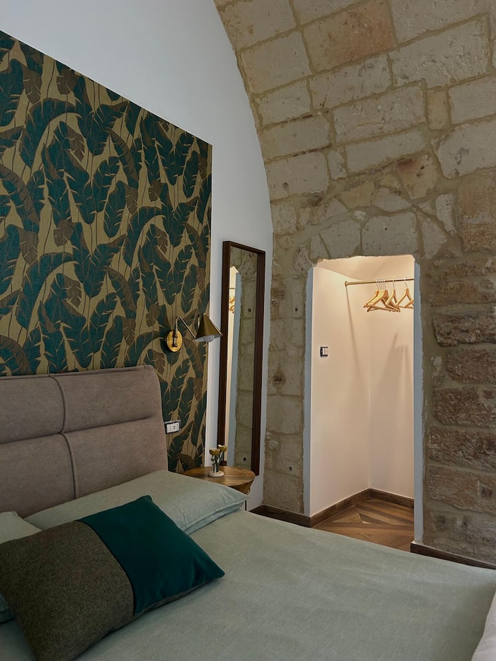 Cama doble envolvente, paredes con papel tapiz botánico y detalles de piedra. Una mezcla perfecta de comodidad y encanto