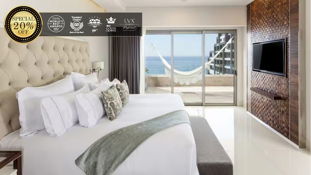 The bedroom features a plush king bed, complemented by a soft gray blanket. A glass door allows natural light and ocean views, leading to a private terrace with a hammock. A wall-mounted flat-screen TV is present across from the bed, enhancing the modern decor.
