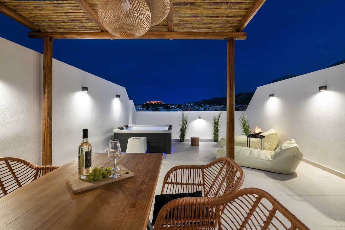 A private terrace is illuminated under the evening sky, showcasing comfortable outdoor furniture including a cozy lounge chair and a wooden dining table. A sleek hot tub is visible, and greenery accents the space. Soft lighting enhances the serene atmosphere for relaxation.