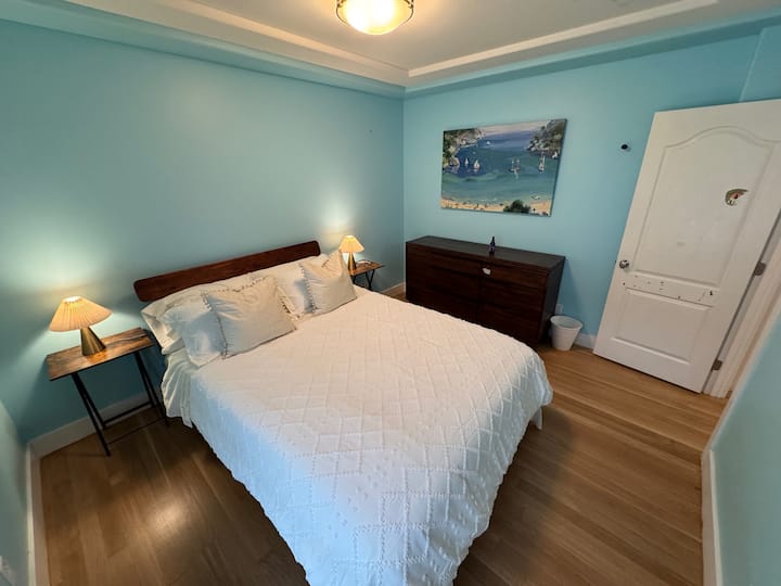 ผ่อนคลายในห้องนอนที่ร่าเริงนี้ด้วยผนังสีน้ำเงินที่สงบ เครื่องนอนที่อบอุ่น และแสงไฟที่อบอุ่นเพื่อการพักผ่อนยามค่ำคืนที่สงบ