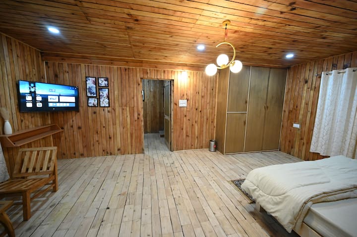 Une chambre douce en bois avec des équipements modernes allie charme rustique et confort, avec un mobilier élégant et une décoration chaleureuse, tout en partageant une salle de bain commune bien équipée.