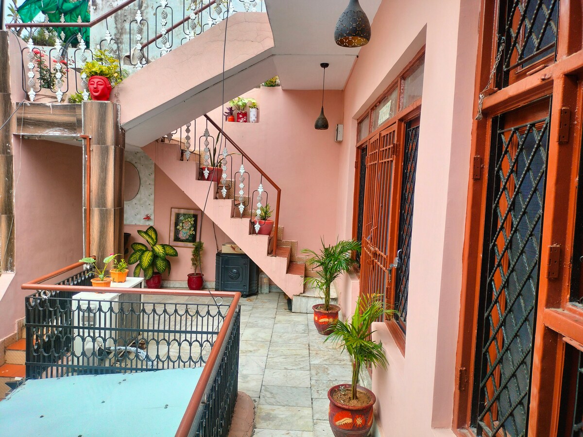 An exterior view showcases a charming staircase adorned with decorative planters. The entrance is framed by multiple windows, allowing natural light to enhance the warm hues of the walls. Potted plants are arranged on the terrace, adding greenery to the space.