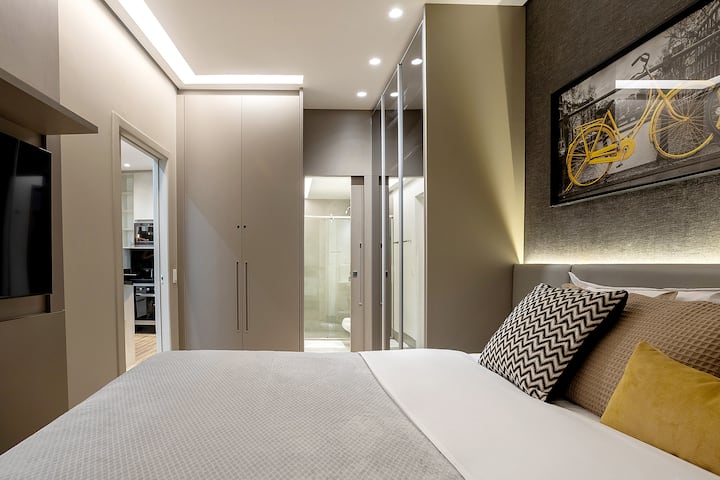 חדר השינה האלגנטי עם מיטת קווין סייז, טלוויזיה, ארונות מתוכננים וגישה ישירה לחדר הרחצה. עיצוב מודרני עם תאורה מובנית ופרטים נעימים שמבטיחים נוחות וסטייל.