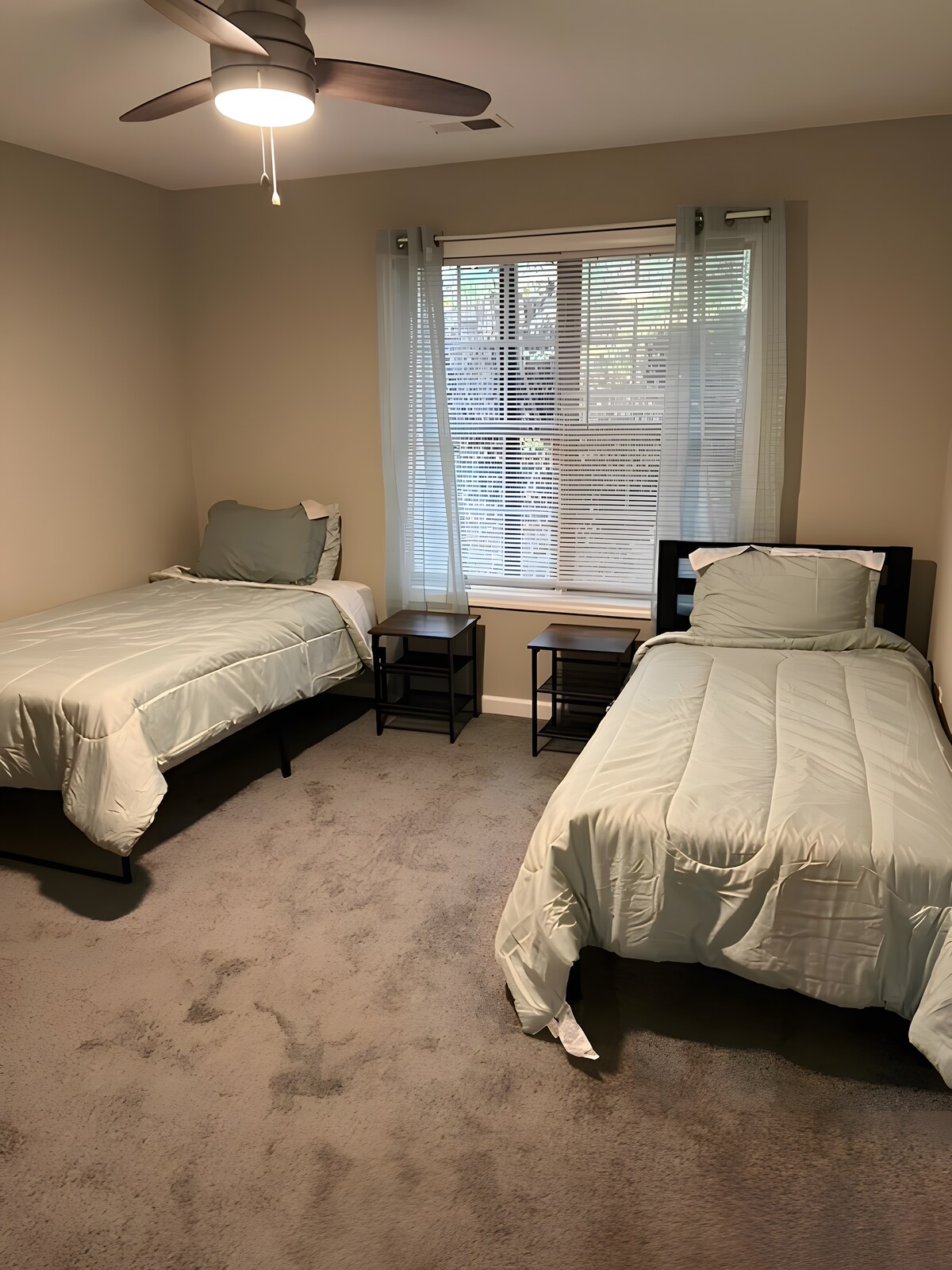 غرفة نوم واسعة بسرير فاخر، مزينة بوسائد زرقاء وأعمال فنية تجريدية على الحائط. تؤدي الغرفة إلى مدخل مع سلالم، مما يضيف عمقًا إلى المساحة الساطعة والبسيطة.