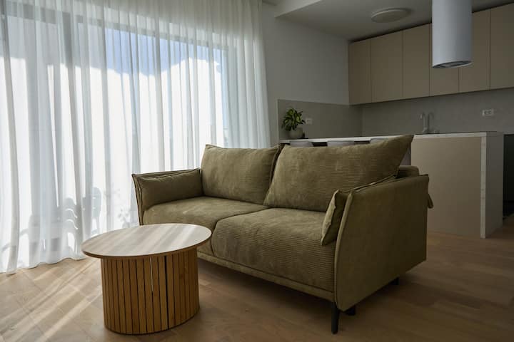 De woonkamer is ingericht in een moderne en gastvrije stijl. In het midden van de kamer is een comfortabele slaapbank met zachte kussens, perfect om te ontspannen of om te veranderen in een extra slaapruimte.