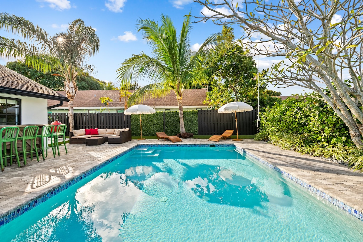 A private pool is surrounded by lounge chairs and tropical plants, inviting relaxation under the blue sky. The area features sun umbrellas and a comfortable seating arrangement, creating an appealing outdoor space for gatherings and leisure.