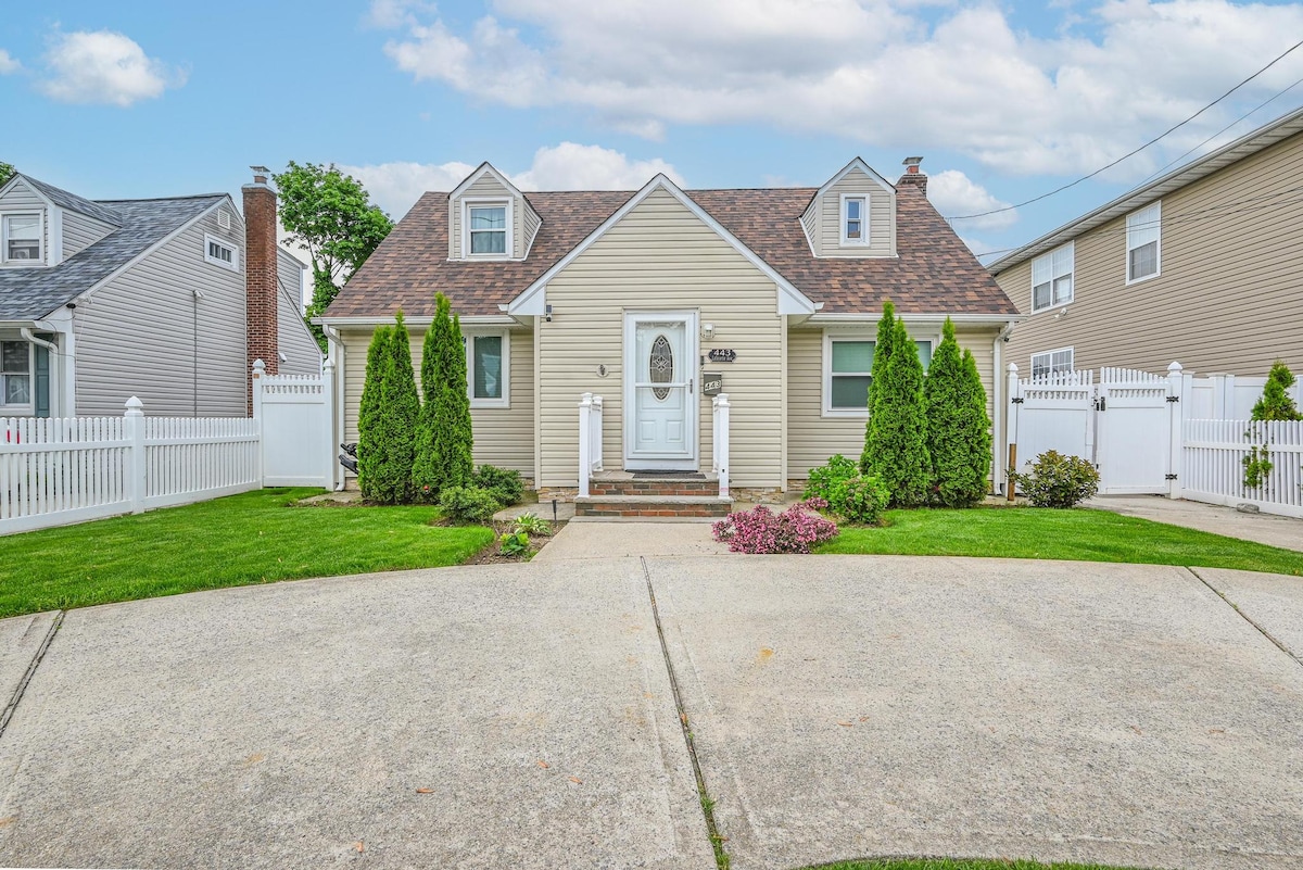 A charming exterior view of the house showcases a tidy front yard, framed by well-maintained green shrubs and blooming flowers. The light-colored siding and neatly shingled roof contribute to the inviting appearance. A concrete driveway leads to the welcoming entrance of the home.