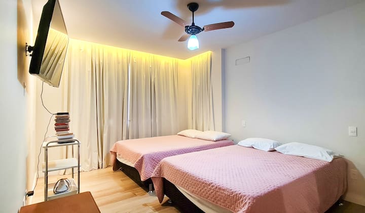 Bedroom 1 equipped with two double beds, ceiling fan, blackout curtains, smart TV with streaming, place to store clothes and bedding.