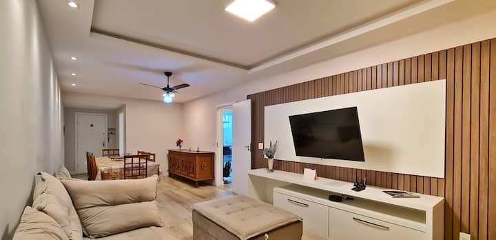 Living room integrated with the dining area, equipped with a spacious sofa, central pouf, ceiling fan, Wi-Fi, smart TV with streaming and blackout curtains, with direct access to the balcony.
