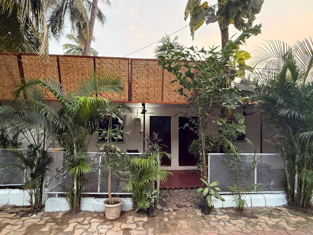 The entrance to the property is framed by lush greenery and well-maintained plants. A mix of tropical and ornamental plants adds to the natural setting, with a charming patio that leads to the front doors. The warm tones of the walls complement the earthy landscape.