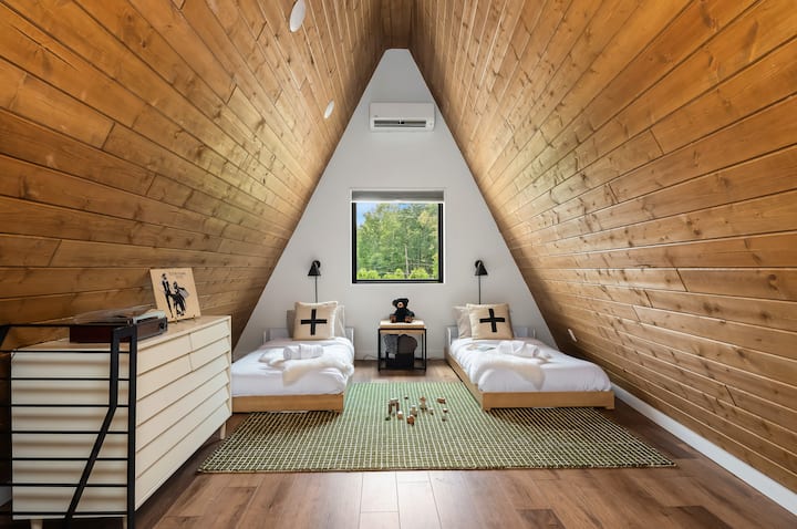 Útulný áčkový domček s dvoma samostatnými lôžkami, drevenými stropmi a centrálnym oknom s výhľadom na stromy. Ideálne pre deti, tínedžerov alebo priateľov – tento flexibilný priestor na spanie uľahčuje uspokojenie potrieb vašej skupiny.